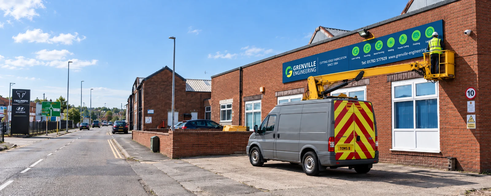 Cherry picker alongside a building during installation of a Grenville Engineering sign