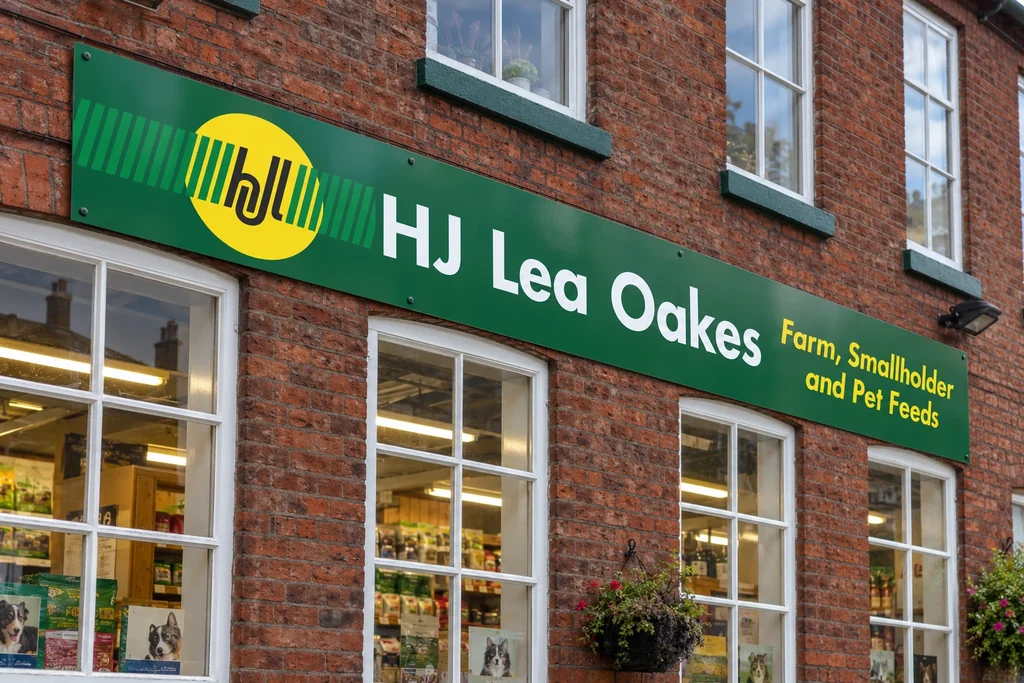 HJ Lea Oakes green 3mm flat fascia with white and yellow graphics mounted on a brick shopfront