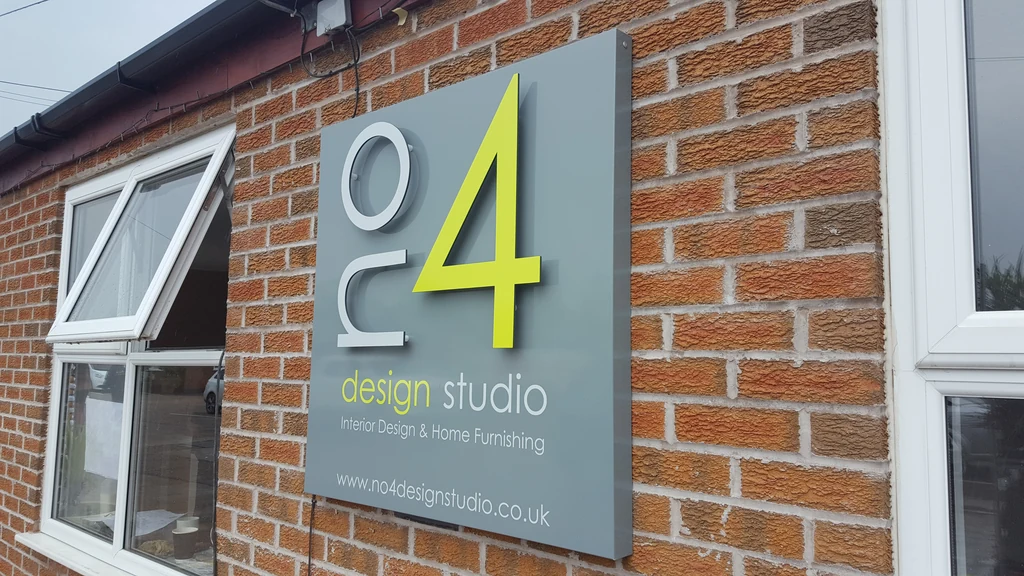 Grey aluminium composite sign tray with raised flat-cut white and lime lettering mounted on a brick wall