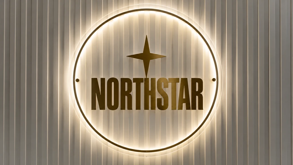 Clear circular NORTHSTAR acrylic logo with gold lettering and a warm white halo on a fluted wall